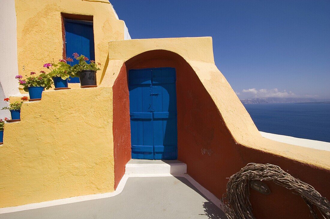 Yellow house, cascading flowerpots, blue door and sea view. Santorini. Greece