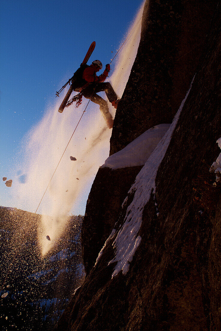 Man rappelling during small avalanche with skis on his back on Donner Summit, California. USA