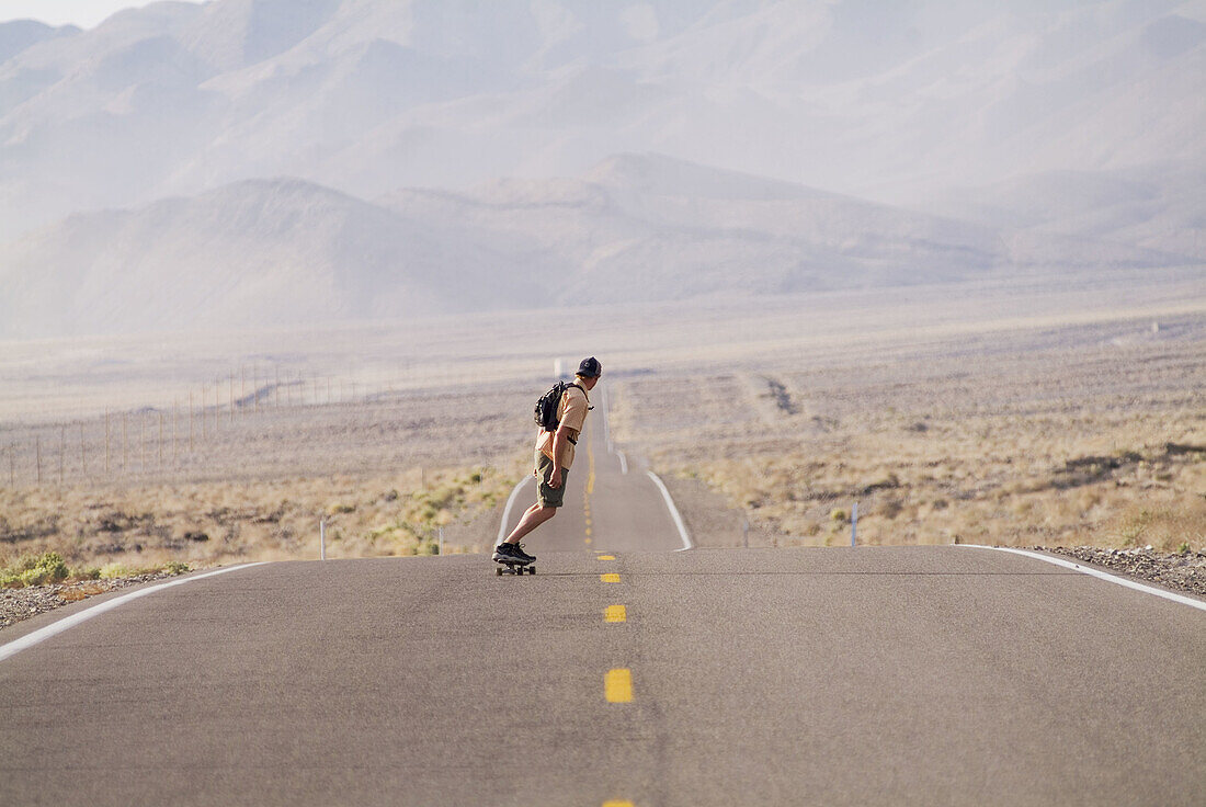 A man skateboarding on a desert road near Lone Pine, California. USA