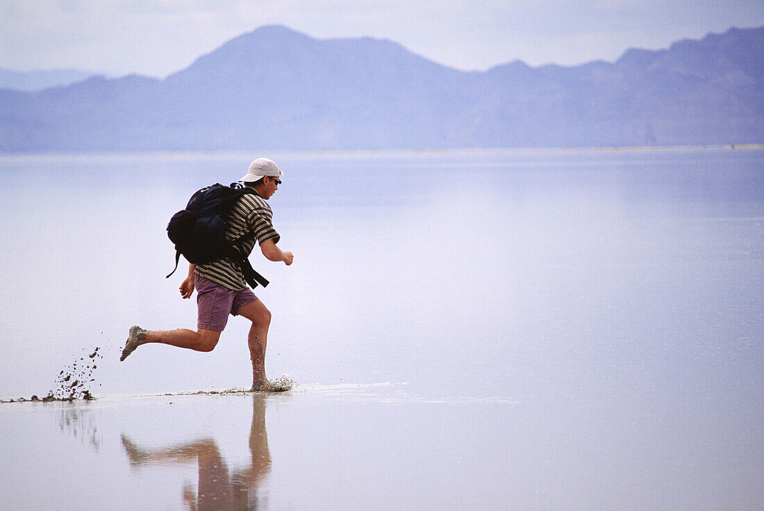 A man hiking across the Bonneville Salt Flats after a summer rain storm.