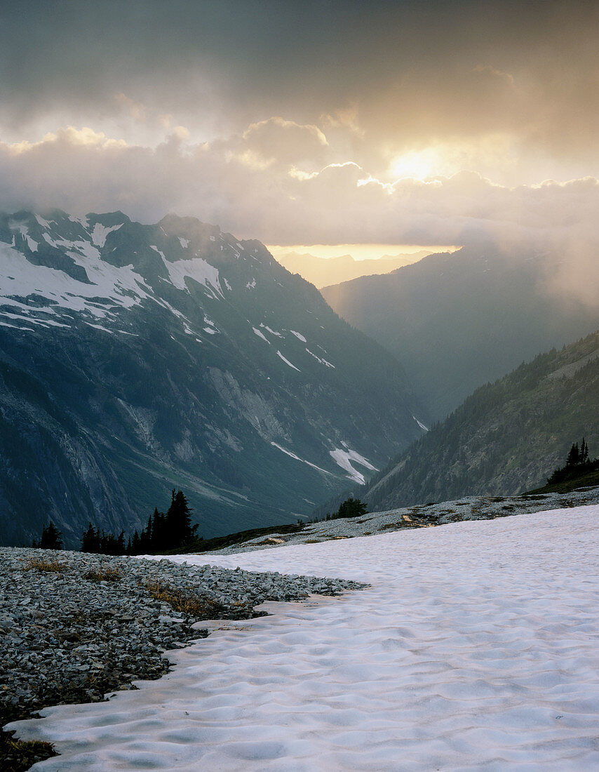 Setting sun through clouds above Ruth Creek Valley. Mount Baker Wilderness. Washington. USA.