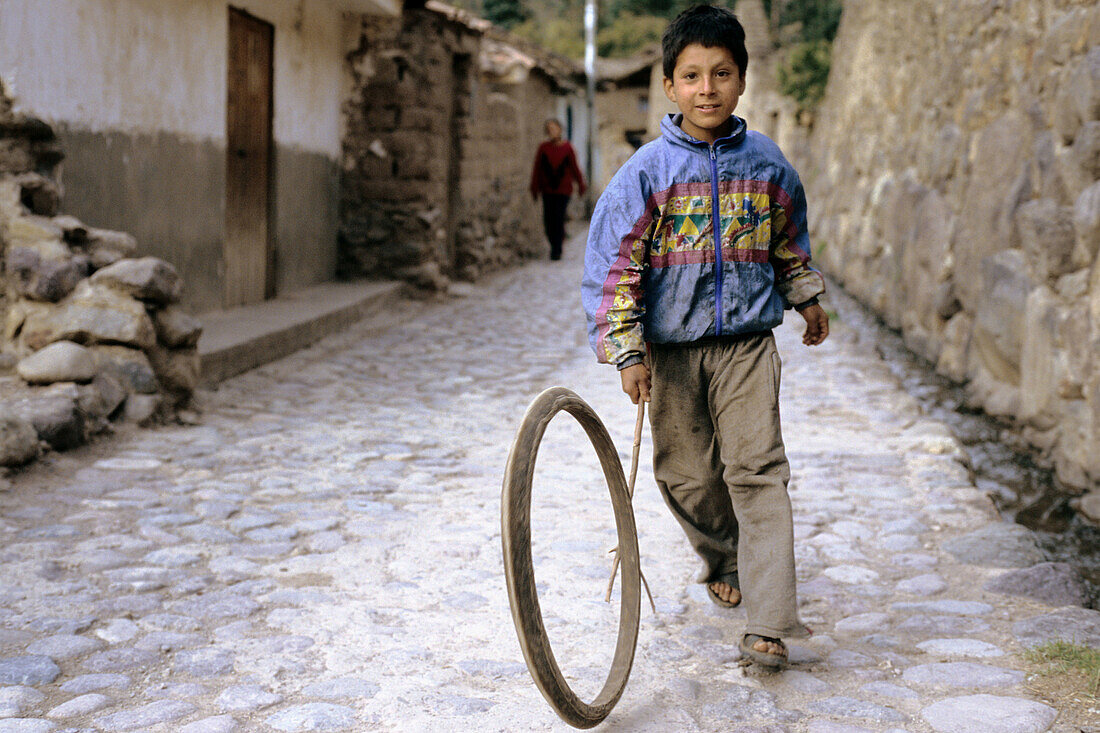 Peruvian boy playing on a narrow cobblestone street from the inca period. Ollantaytambo, Perù.