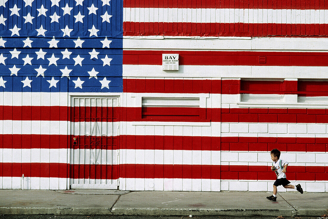 Child running in front of US flag painted on wall. California, USA