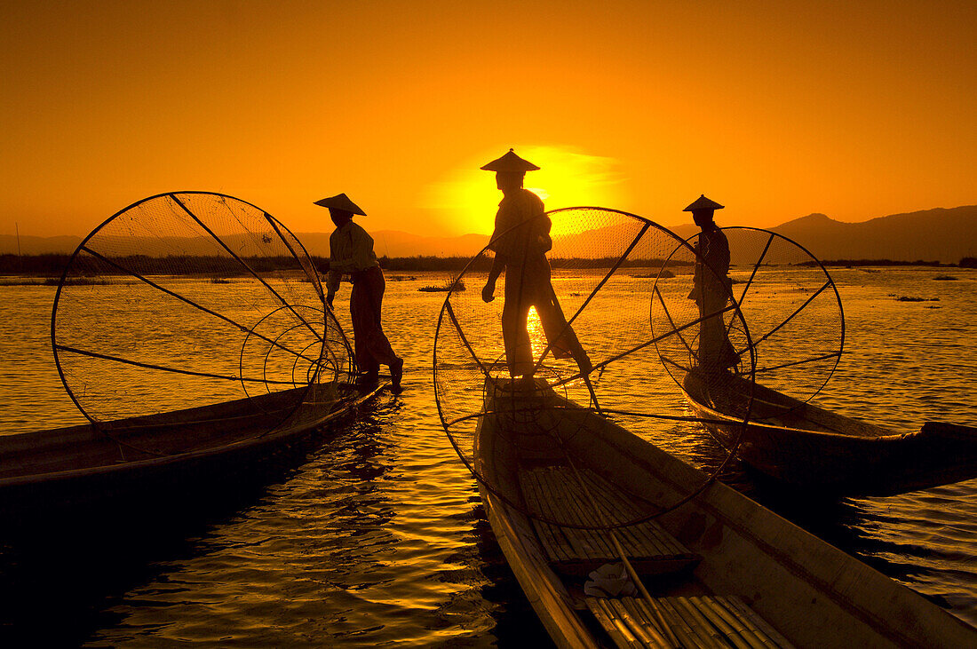 Legrower fisherman set conical traps as the setting sun reflects on Inle Lake, Shan State, Myanmar (Burma)