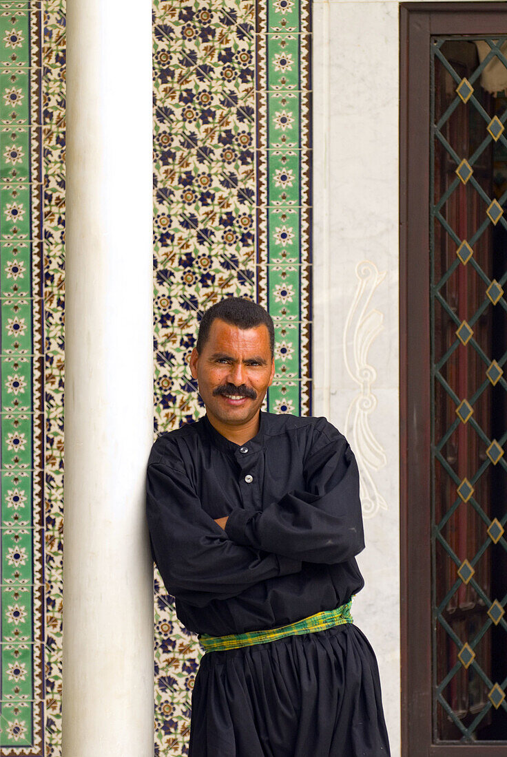 Tunisian man standing in front of a tiled wall in a courtyard at the Dar Cherait Hotel and Museum, Tozeur, Tunisia
