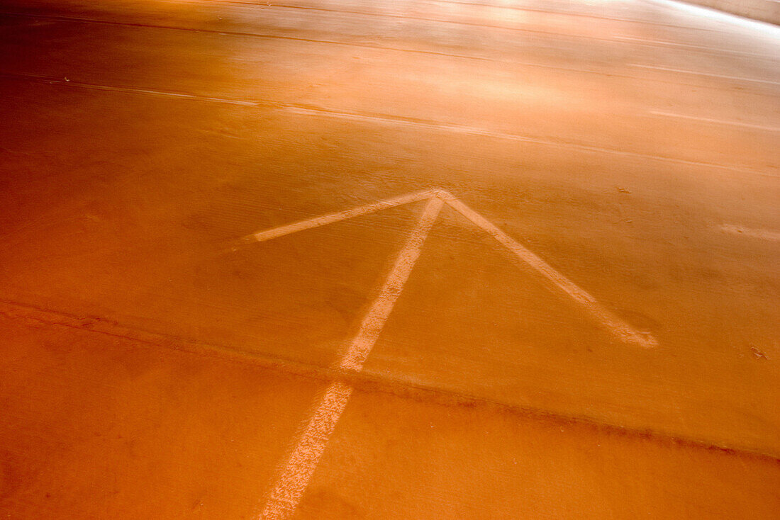 Traffic direction arrow painted on the floor of a parking garage.