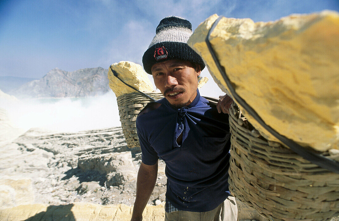 Miner with heavy load of yellow elemental sulphur collected from within the active crater of Volcano Ijen, eastern Java, Indonesia