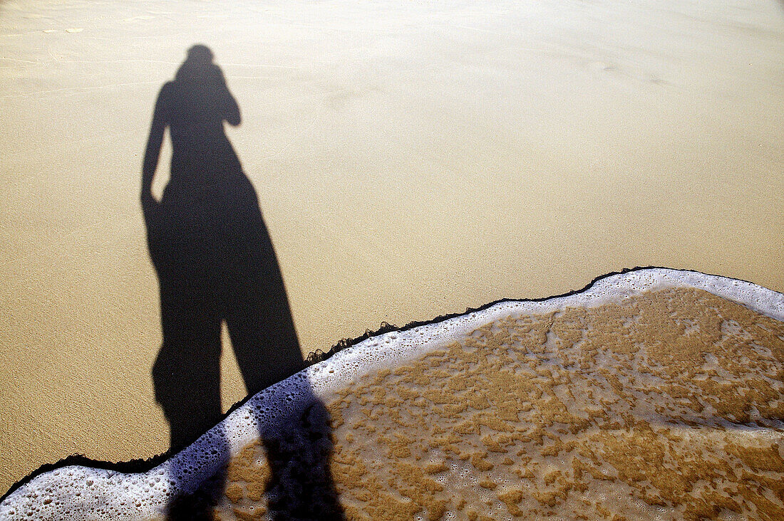 Shadow of woman standing in the waves on white sand beach
