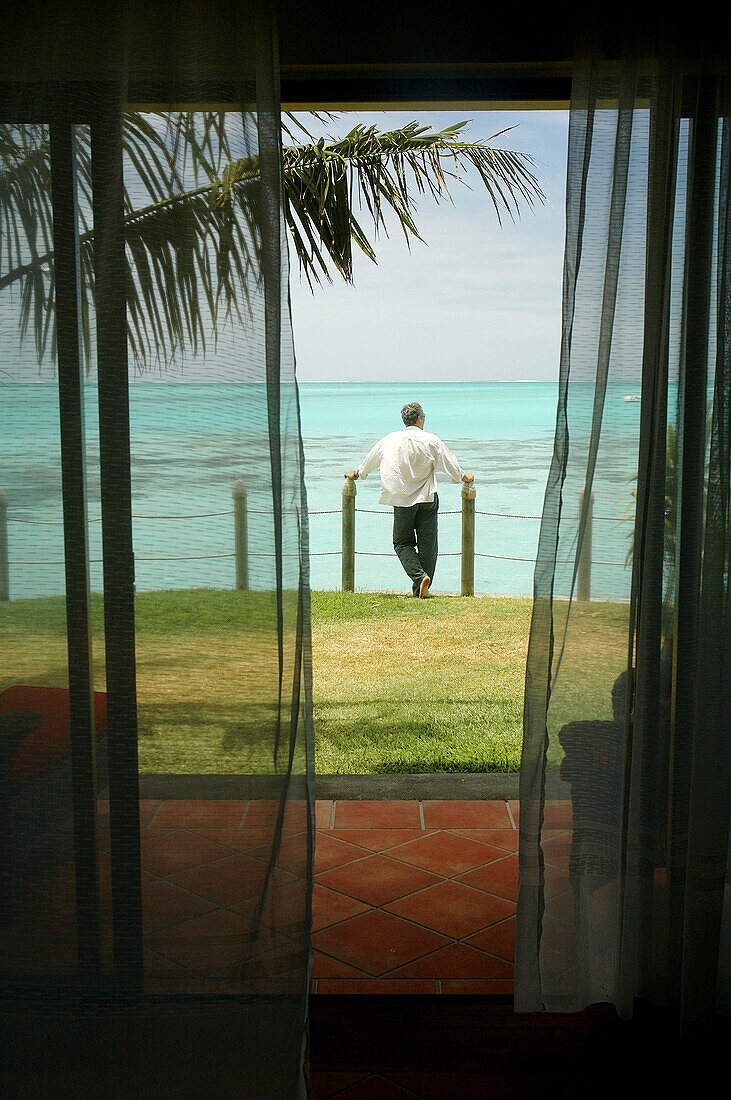 Man overlooking tropical turquoise lagoon out the front of his luxury resort bungalow.