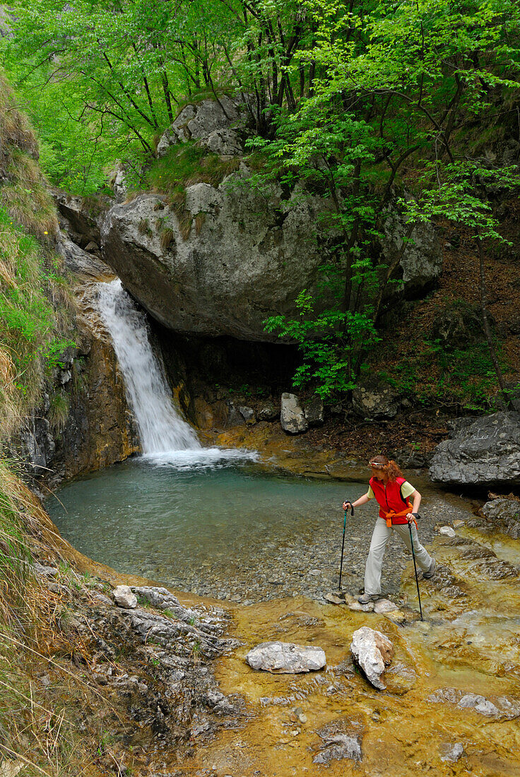 young woman crossing stream with waterfall, Valle di Era, Mandello, Somana, lake Comer See, Como, Lombardy, Italy