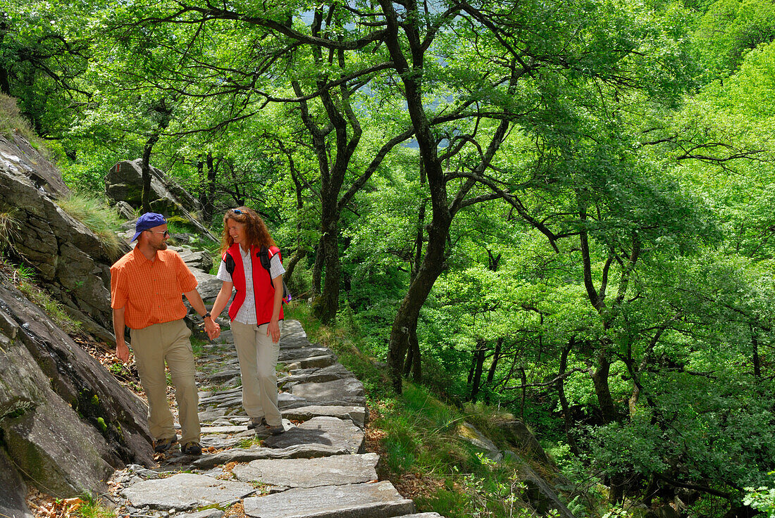 junges Paar auf Steinplattenweg unter Laubbäumen, Tessin, Schweiz