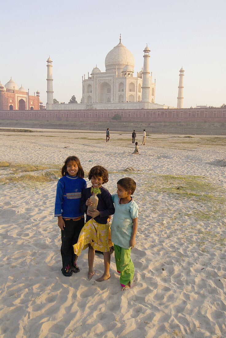 Kids standing in the sand, with group of boys playing cricket in the background, near the banks of the Yamuna River, Taj Mahal, Agra, Uttar Pradesh, India