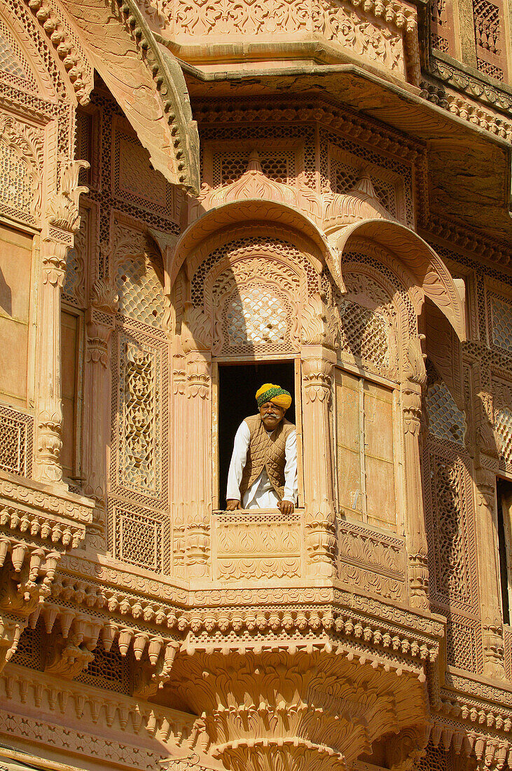 Rajasthani man looking out a window surrounded by an ornate facade at the Mehrangarh Fort, Jodhpur, Rajasthan, India