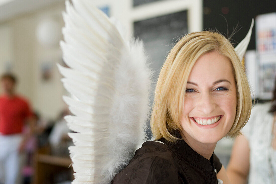 Mid adult woman wearing angel wings sitting in a cafe
