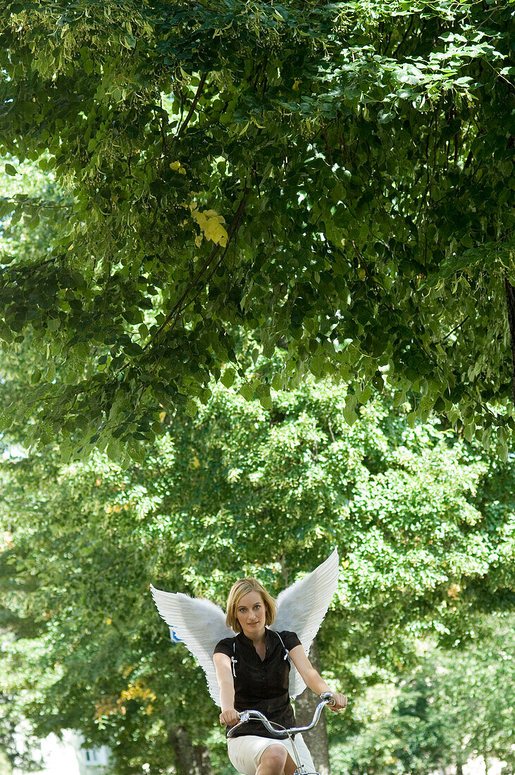 Engel, junge Frau mit Engelsflügeln beim Fahrradfahren, München, Bayern, Deutschland