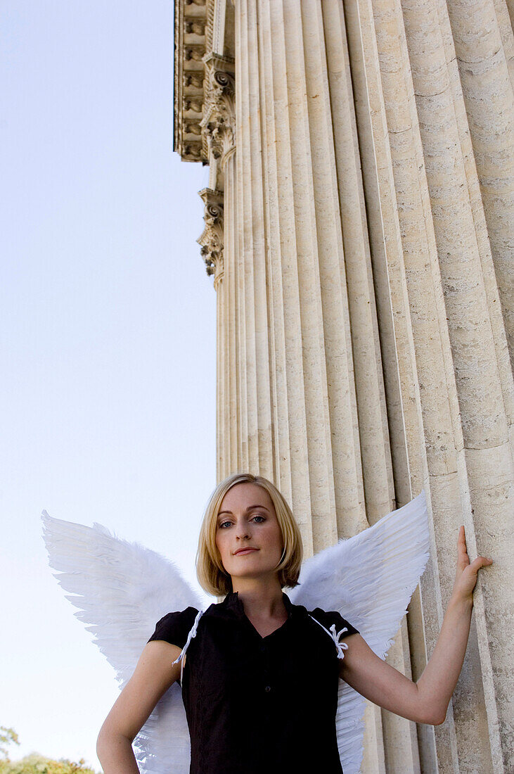 Mid adult woman wearing angel wings leaning against column, Konigsplatz (King's Square), Munich, Bavaria, Germany
