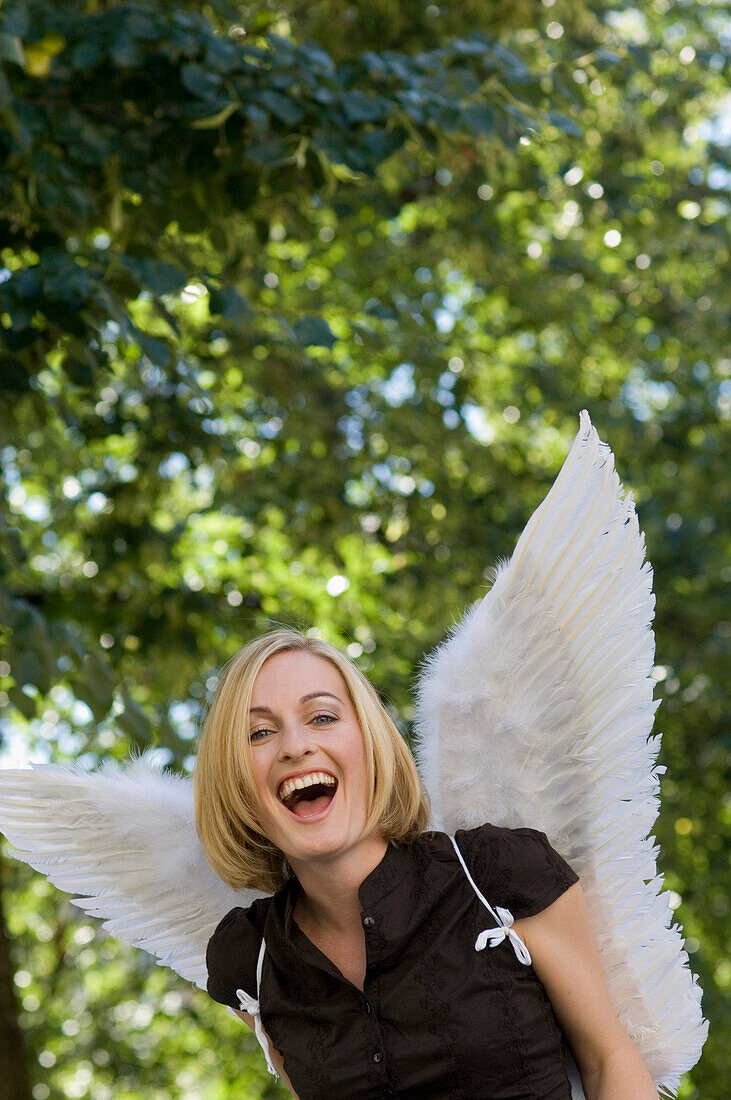 Mid adult woman wearing angel wings laughing at camera