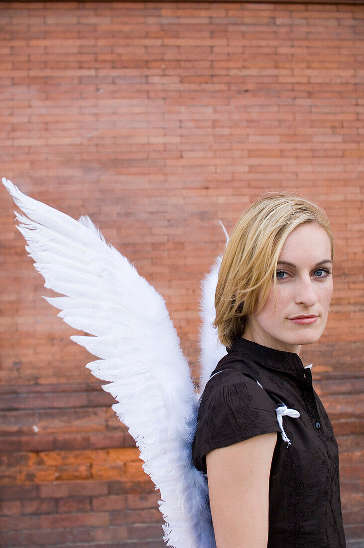 Mid adult woman wearing angel wings in front of a brick wall