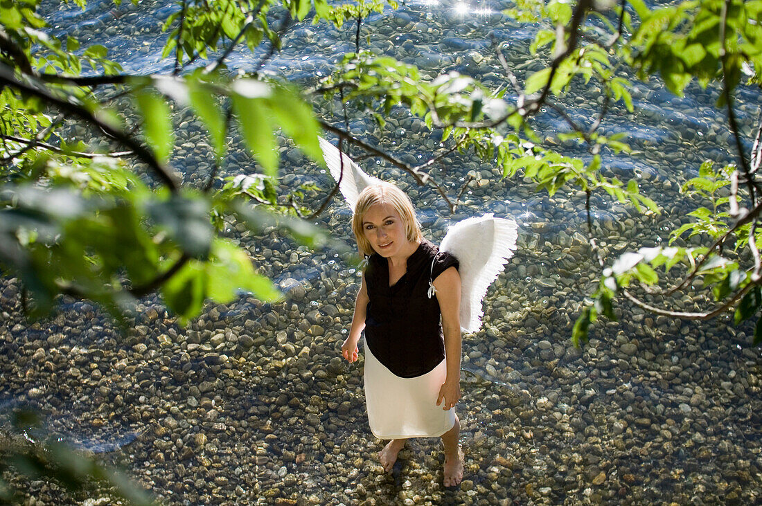 Mid adult woman wearing angel wings standing in lake Starnberg looking up, Bavaria, Germany