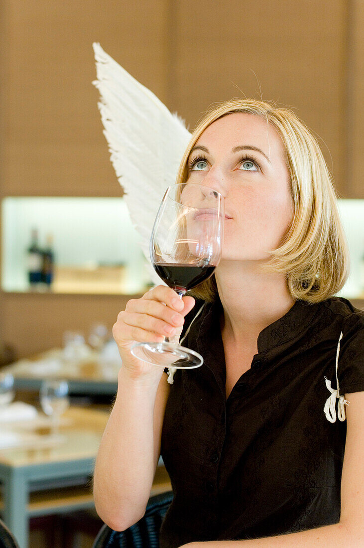 Angel, young woman with wings drinking a glass of red wine, restaurant, Munich, Bavaria, Germany