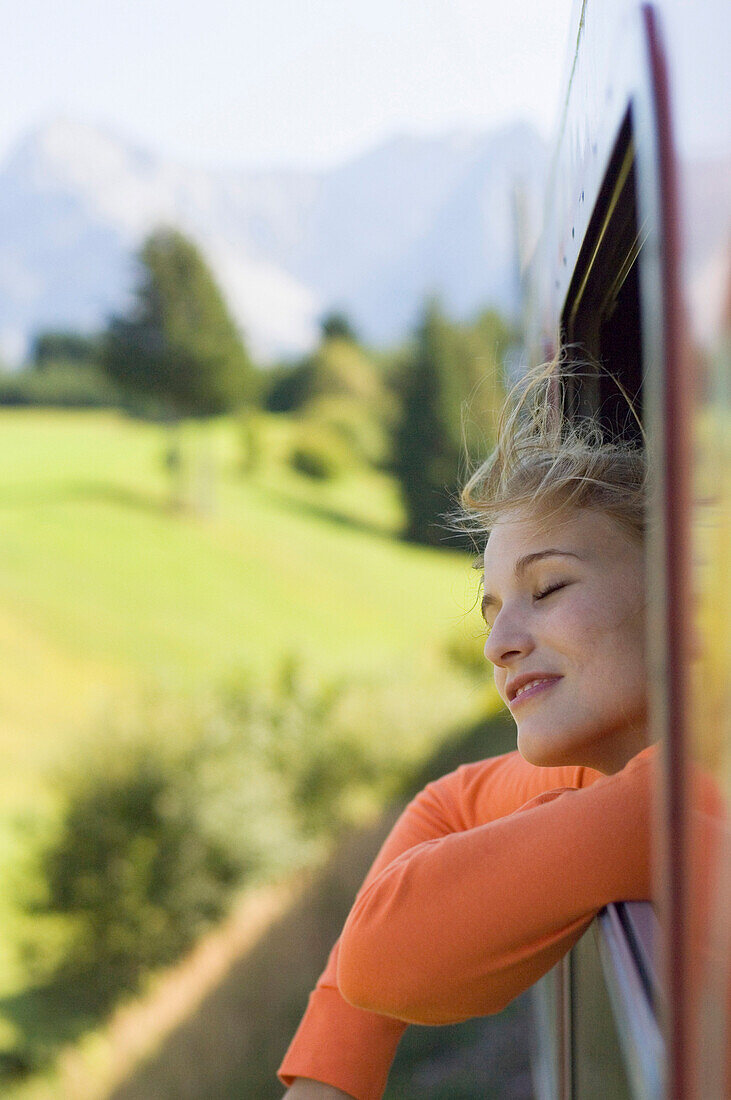 Young woman with closed eyes leaning out a window of speeding train