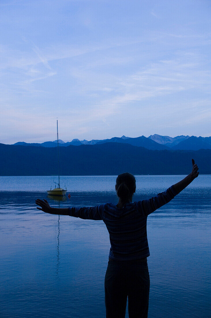 Young woman stretching a lake Walchensee in dusk, Bavaria, Germany