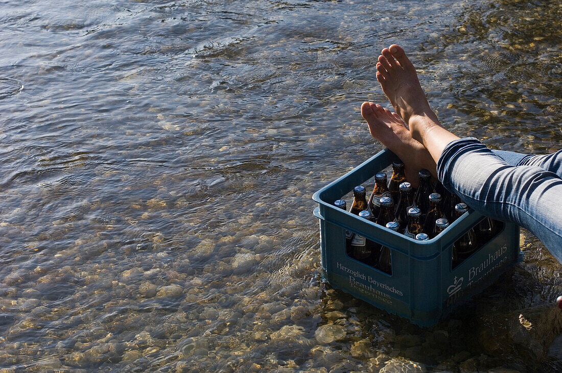 Person resting his feet on a crate of beer, River Isar, Munich, Bavaria, Germany