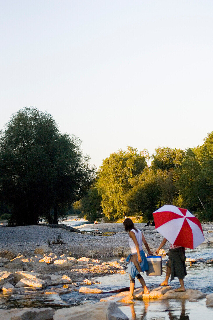 Two young women carrying cooler, picnic on the river Isar, Munich, Bavaria, Germany