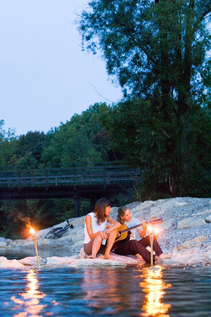 Two young women sitting at river Isar in the evening, Munich, Bavaria, Germany