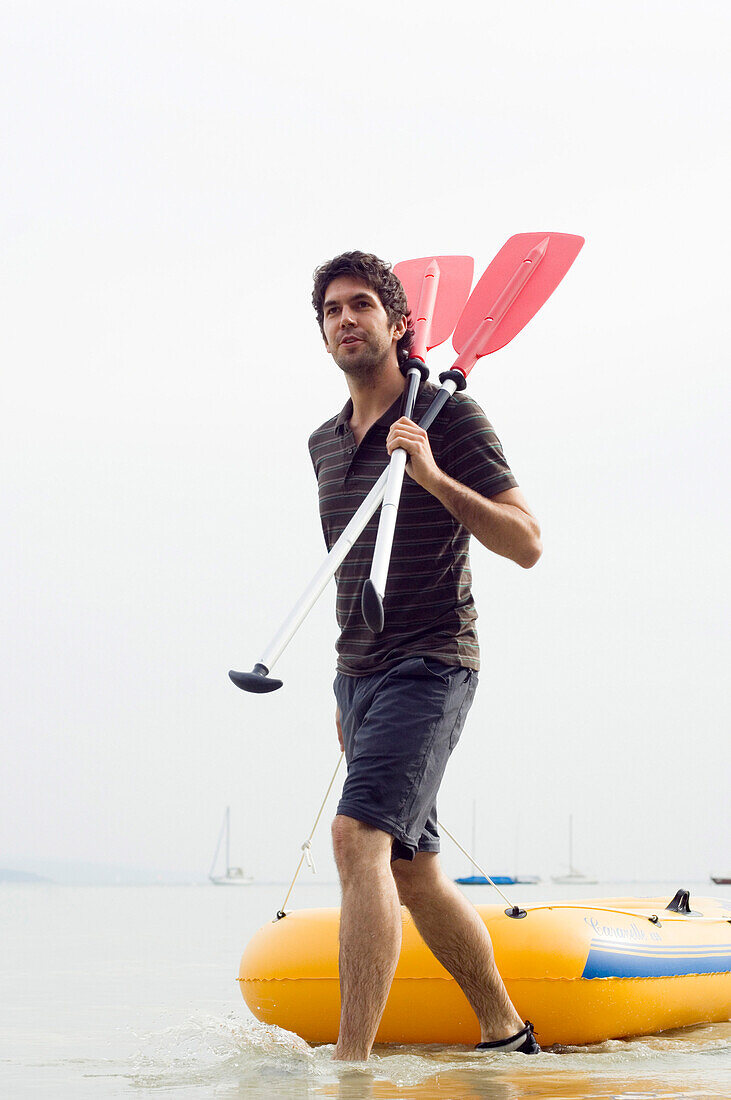 Young man pulling dinghy, lake Ammersee, Bavaria, Germany