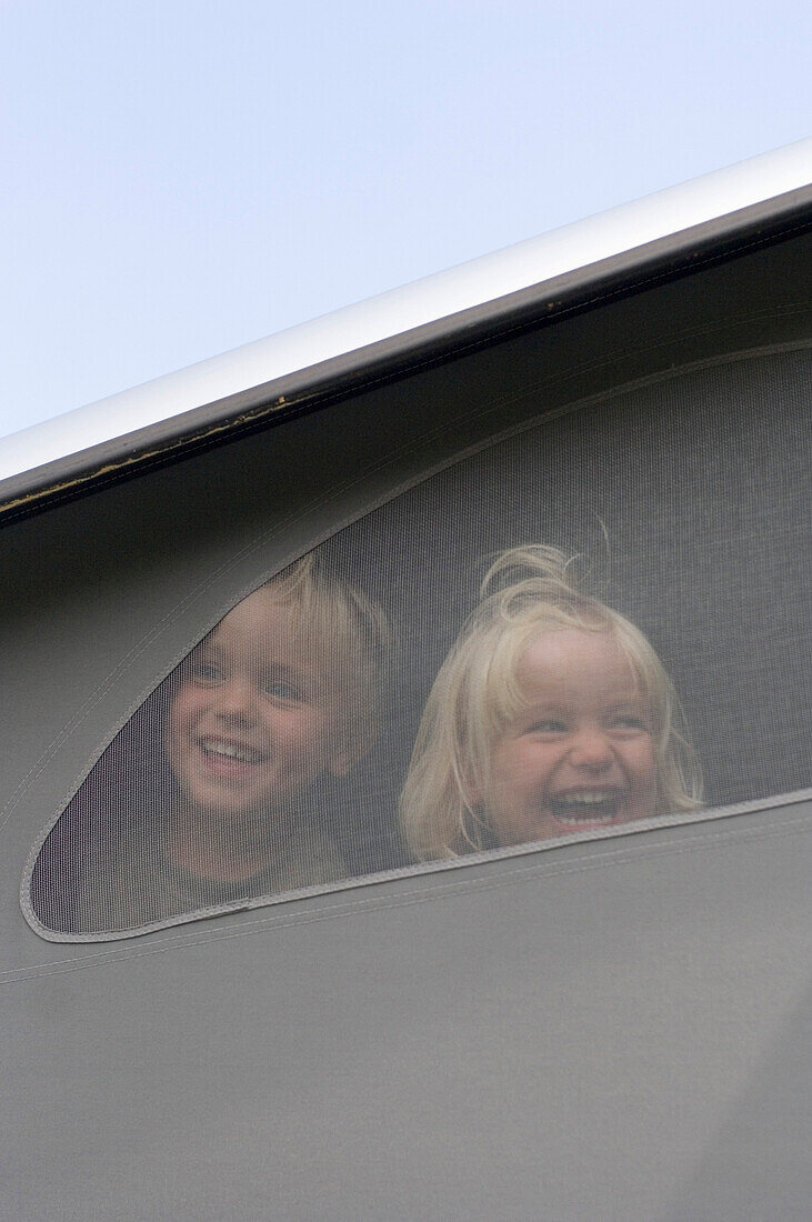 Zwei Kinder (3-4 Jahre) schauen aus einem Wohnmobil