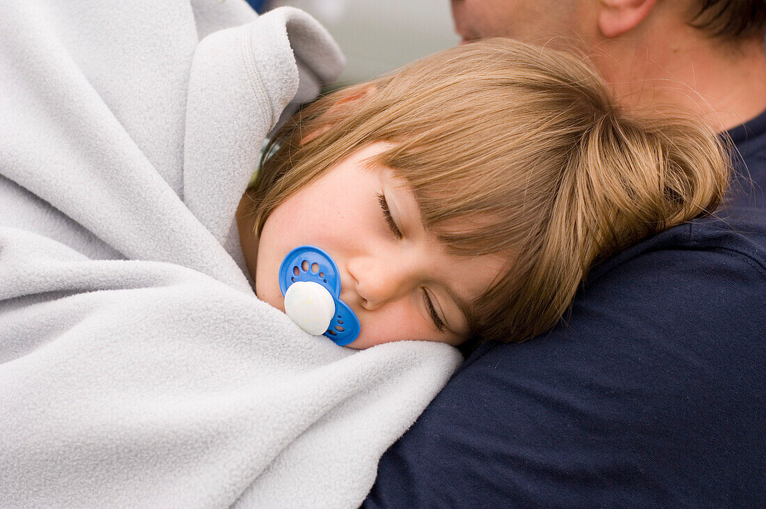 Young girl (4-5 years) asleep on her fathers shoulder, wrapped in a blanket, Bavaria, Germany