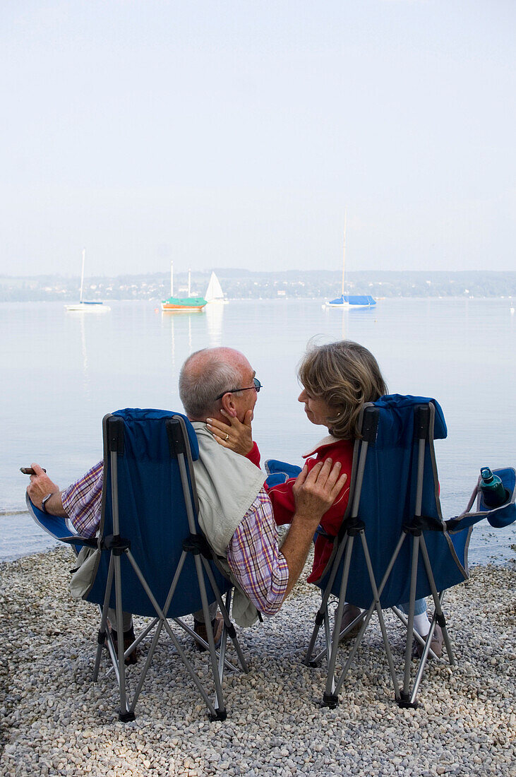 Senior couple sitting in folding chairs at lake Ammersee, Bavaria, Germany