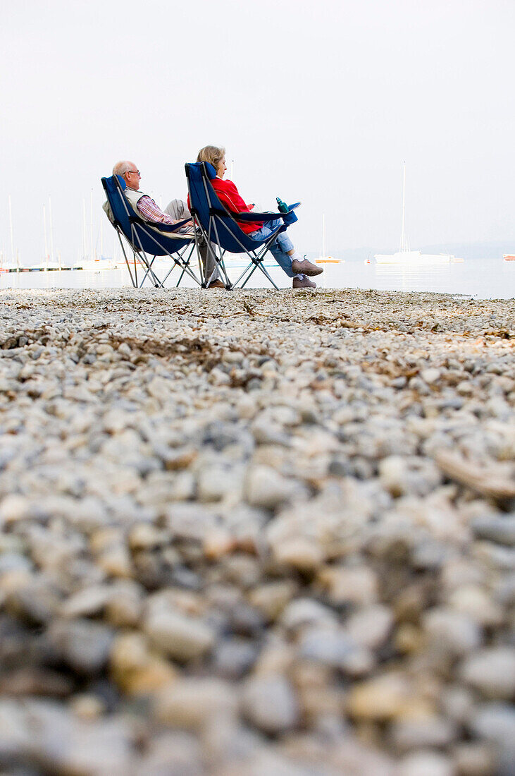Senior couple sitting in folding chairs at lake Ammersee, Bavaria, Germany