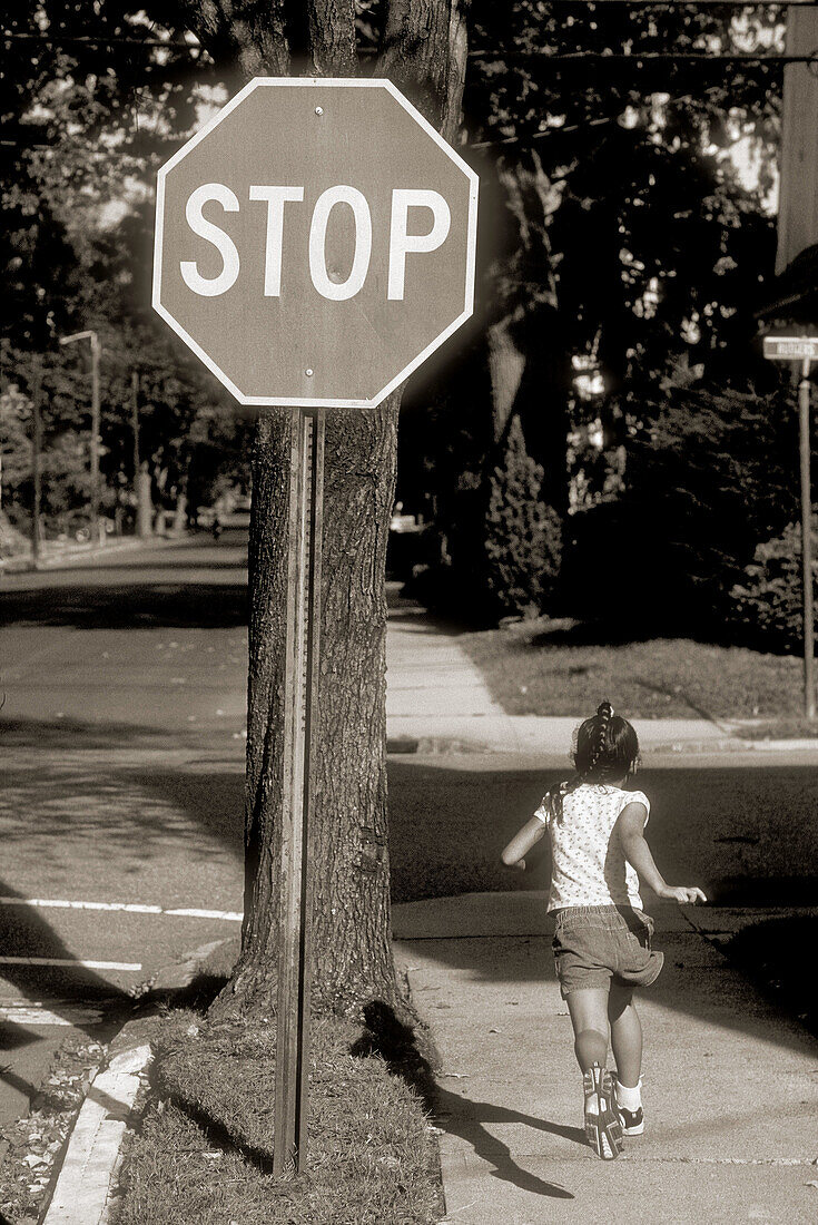 6 year old girl running past stop sign in town of Maplewood. New Jersey, USA