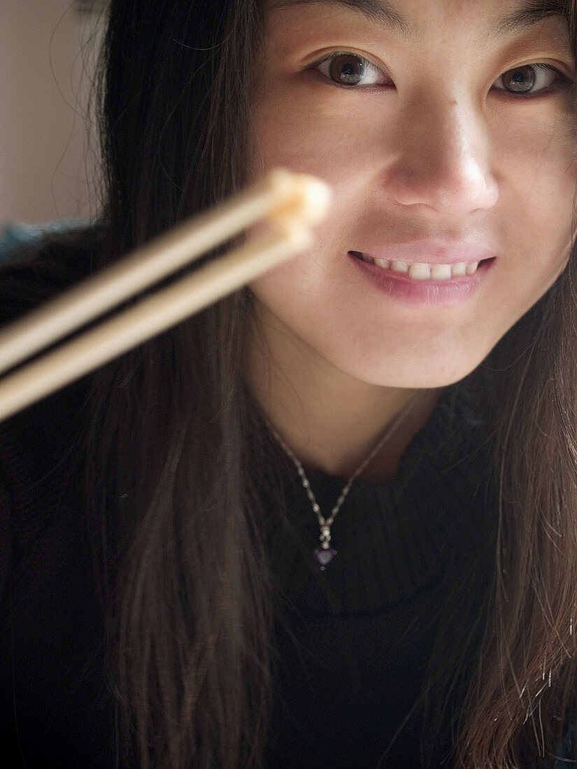 Good looking Chinese girl in black holding a seed of corn with chopsticks