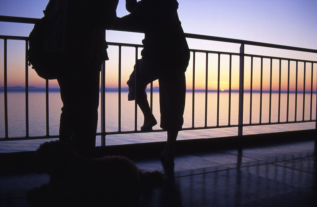 Sunrise seen from a ship going from Barcelona to Menorca with two people silhouettes in the deck, leaning on the handrail. Arriving to the island. Spain.