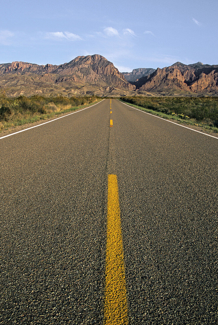 A long stretch of blacktop reaches for the Chisos Mountains on the horizon in Big Bend National Park, Texas, USA.