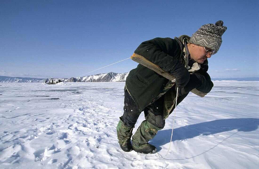 Fisherman pulling net out of an ice hole on frozen Baikal lake in winter, Siberia, Russia