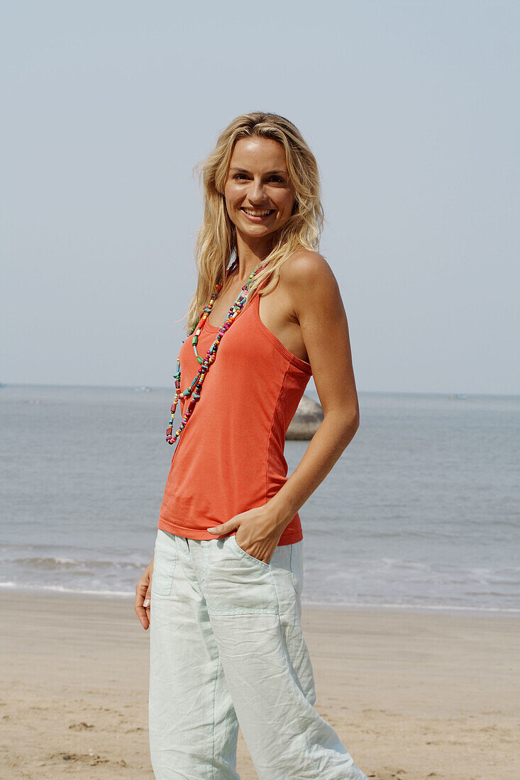 Portrait of a beautiful blonde woman wearing an orange vest and smiling on a beach in India.