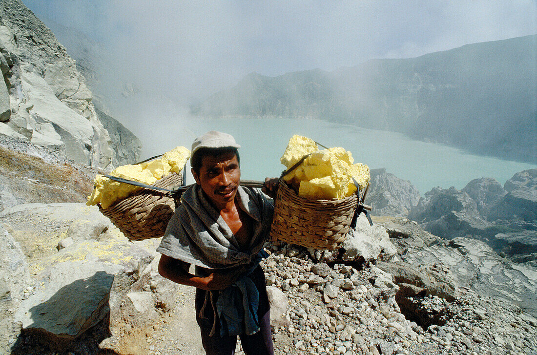 Miner with heavy load of yellow elemental sulphur collected from within the active crater of Volcano Kawa Ijen. Eastern Java, Indonesia