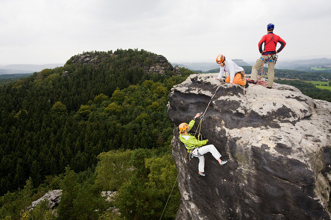 drei junge Menschen, eine Frau und  zwei Männer klettern an den Felsen mit Namen Papststein, Elbsandsteingebirge, Sächsische Schweiz, Sachsen, Deutschland, MR