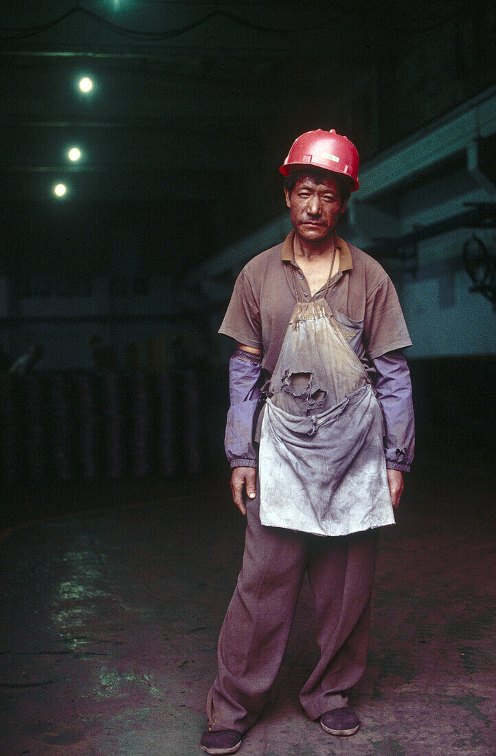 A factory worker in Beijing takes a break from work. His clothes are dirty from the work, manufacturing car parts, outside Beijing. China.