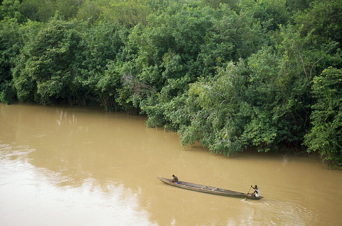 Wooden canoe with two people in it sailing on a brown river. Ivory Coast