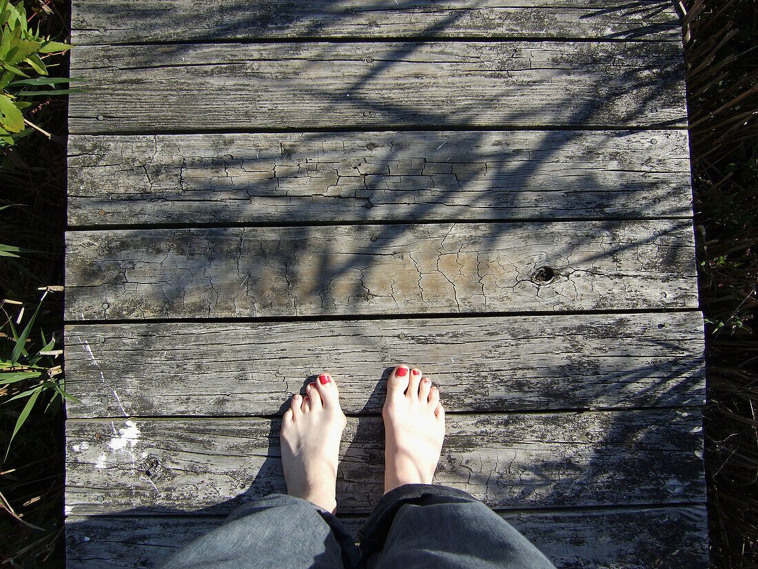Bare feet on a dock in Mattituck, NY. Mattituck is on the South Shore of the North Fork of Long Island. The feet are of a woman, with half worn polish, and bunions, on a sunny day with her jeans rolled up. USA.