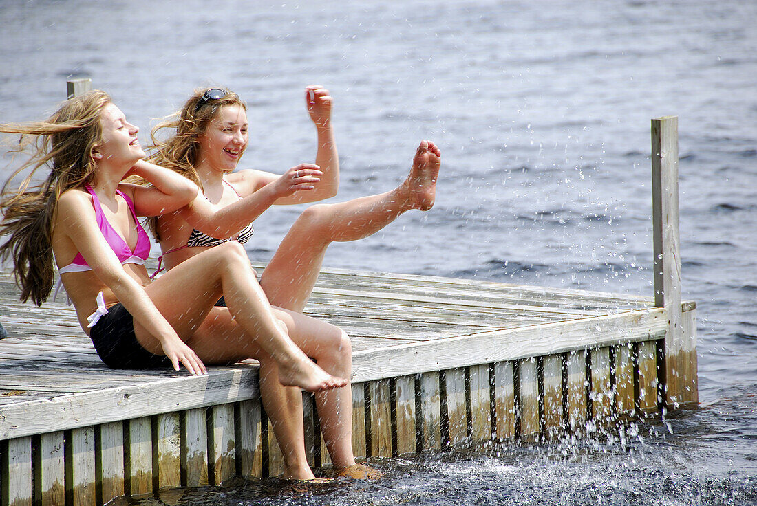 sisters 13 and 18 kicking up water while sitting on dock at lake