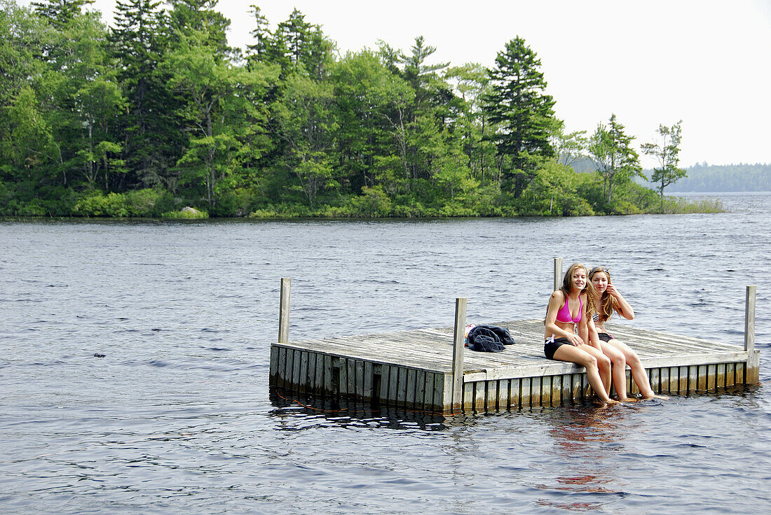 sisters 13 and 18 yrs sitting on dock together at cottage