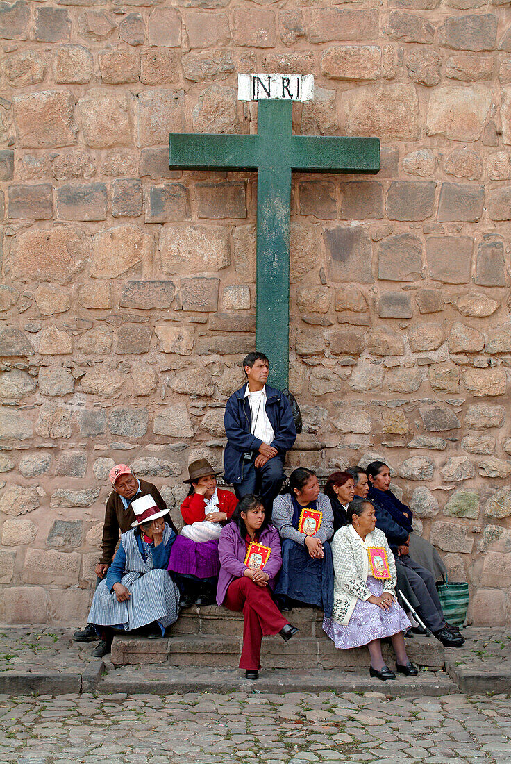 Indigenous believers sitting in front of a cross at the cathedral of Cusco, Peru, South America