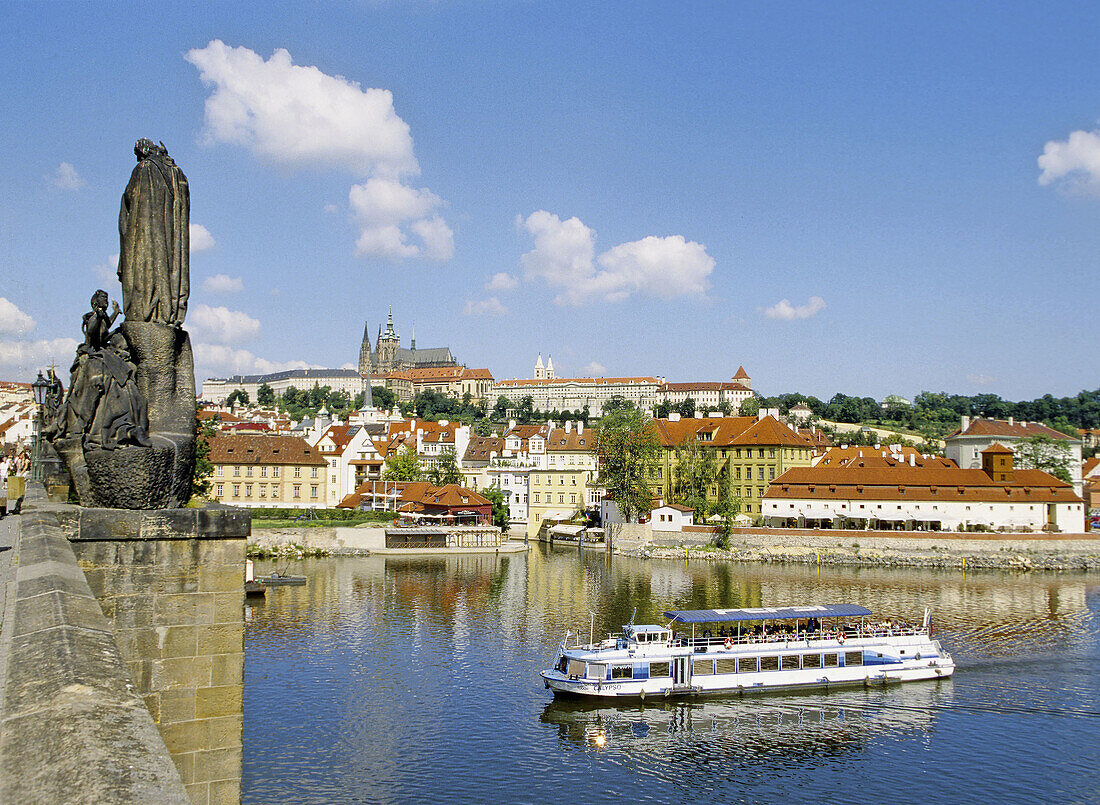 Tourist boat on Vltava River and  Castle from Charles Bridge in Prague, Czech Republic