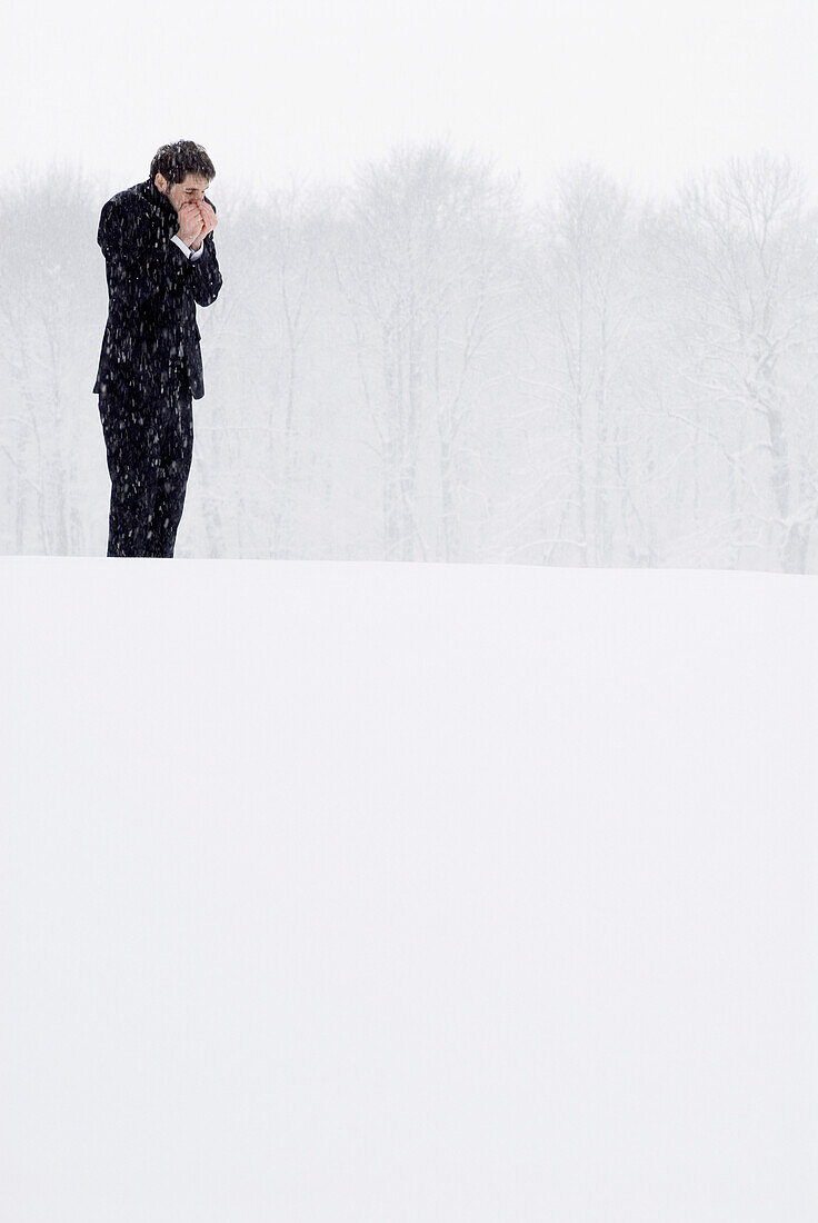Mann im Anzug steht im Schneetreiben und wärmt seine Hände, Englischer Garten, München, Bayern, Deutschland